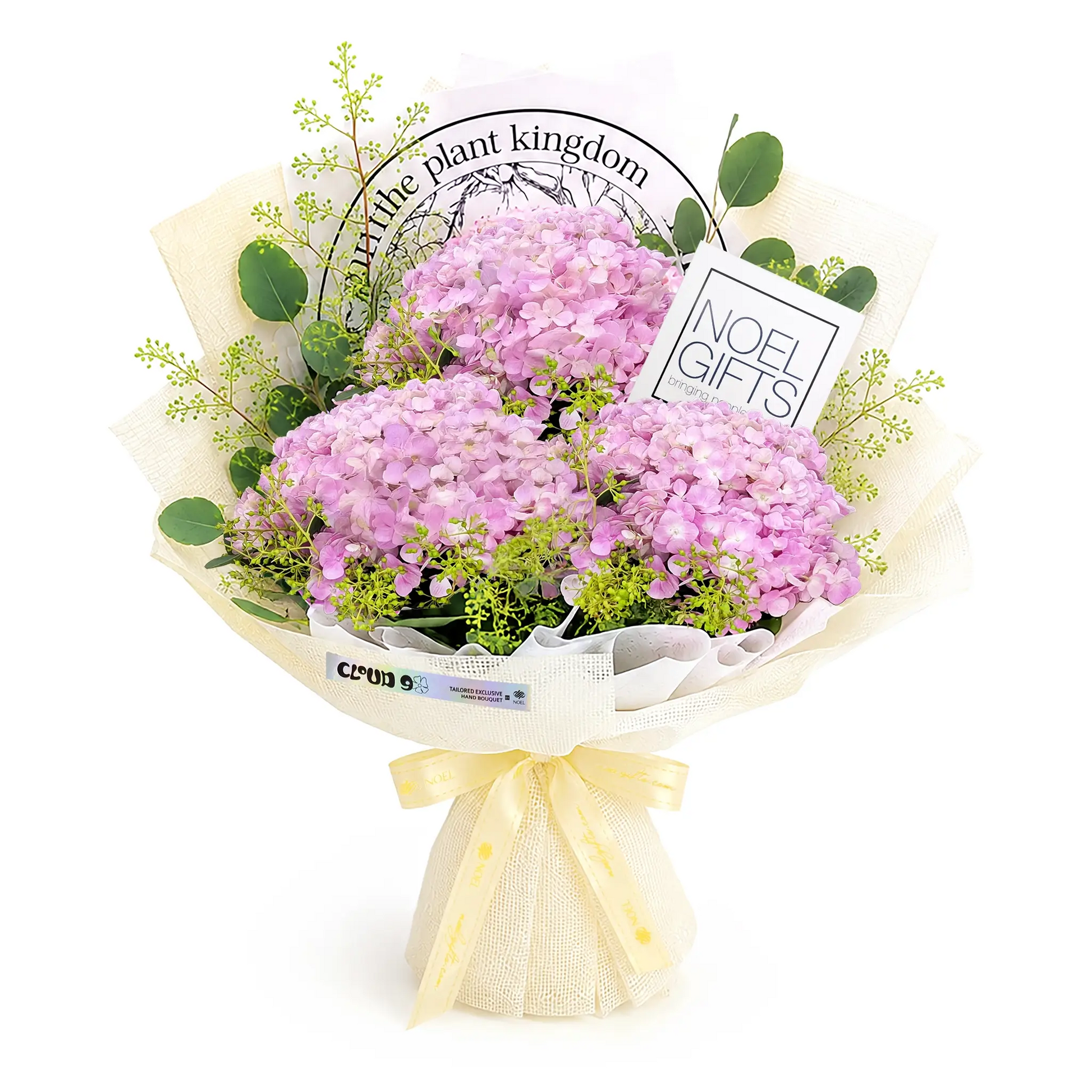 A wrapped bouquet of pink hydrangea flowers with green foliage, tied with a cream ribbon, and styled with a card that reads 'in the plant kingdom' and another that says 'NOEL GIFTS'.