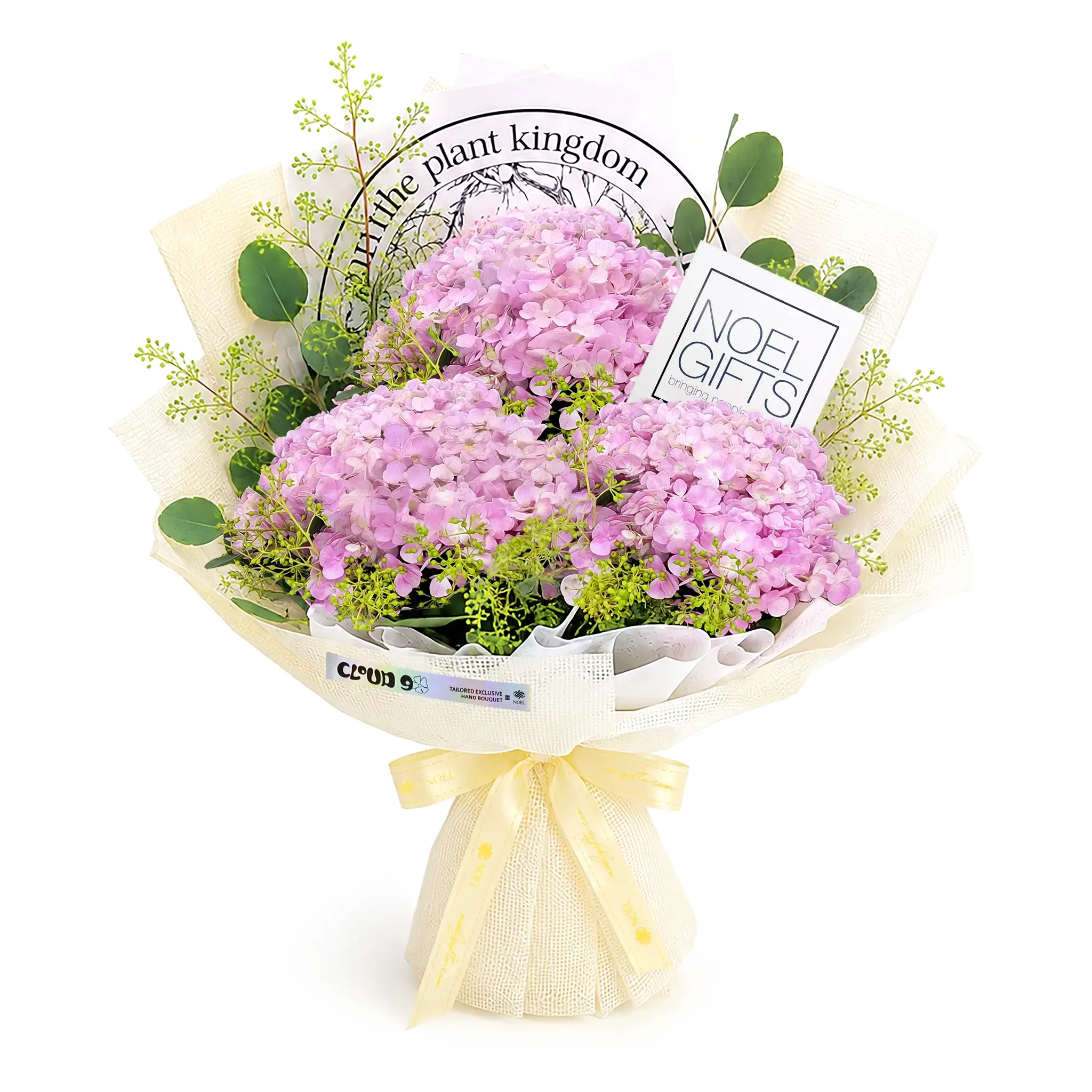 A wrapped bouquet of pink hydrangea flowers with green foliage, tied with a cream ribbon, and styled with a card that reads 'in the plant kingdom' and another that says 'NOEL GIFTS'.