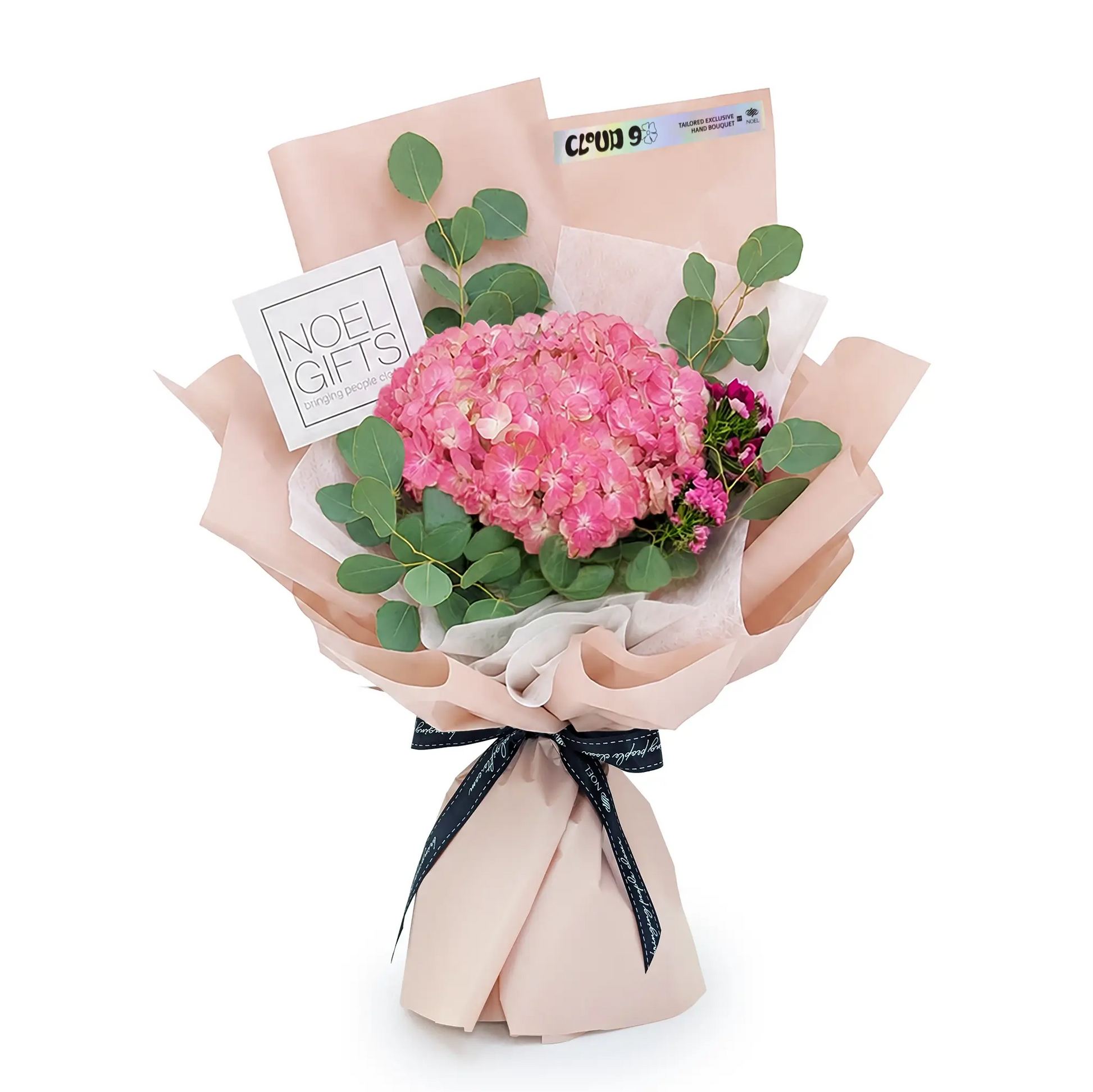 A wrapped flower bouquet featuring a large pink hydrangea cluster, green eucalyptus leaves, and small dark pink flowers, wrapped in blush pink paper with a dark blue ribbon and two gift cards, on a white background.