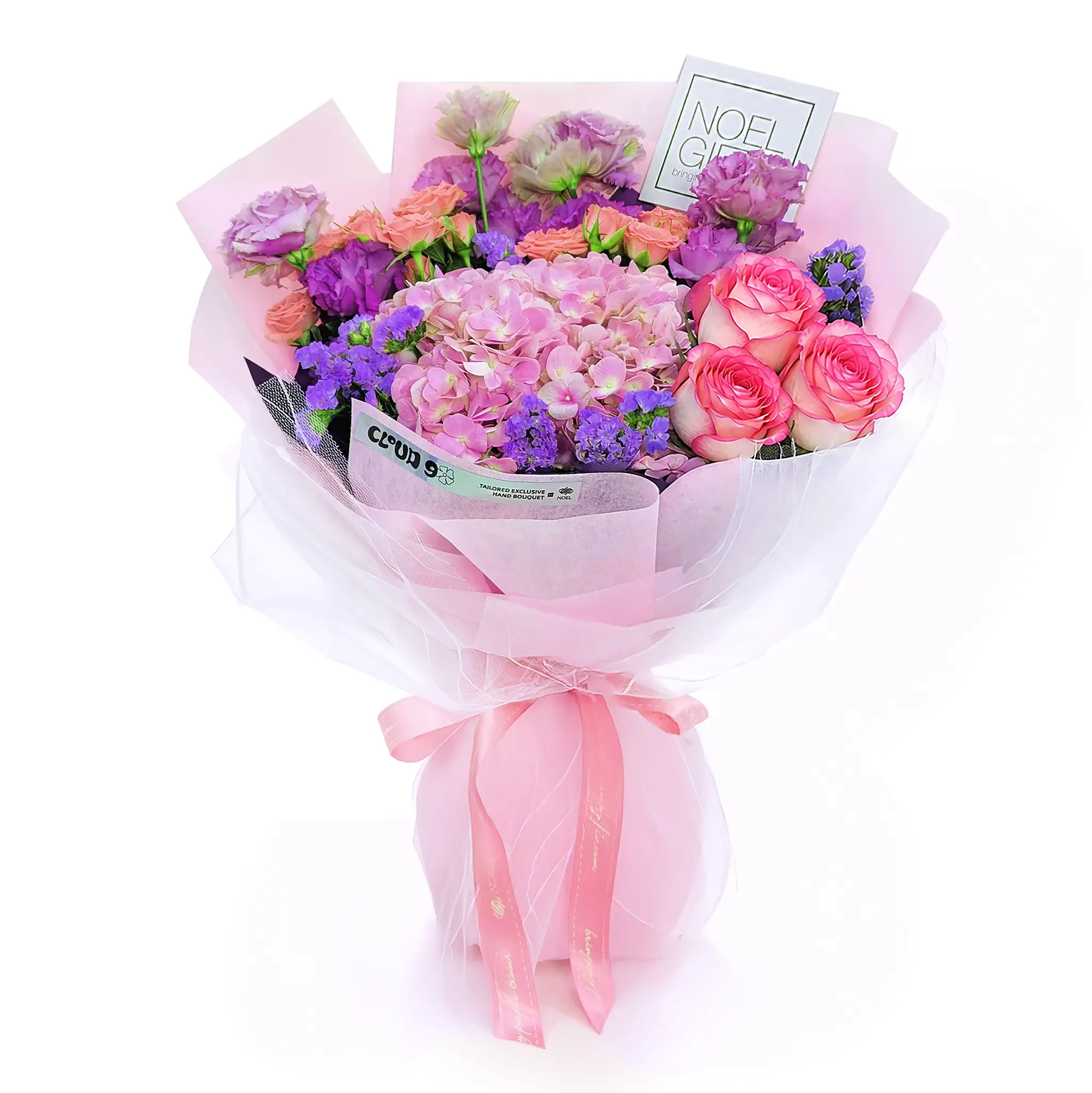 A vibrant floral bouquet wrapped in pink tissue paper and a pink ribbon, featuring pink roses, purple hydrangeas, and purple flowers, with a small card that reads 'NOEL GIFT'.
